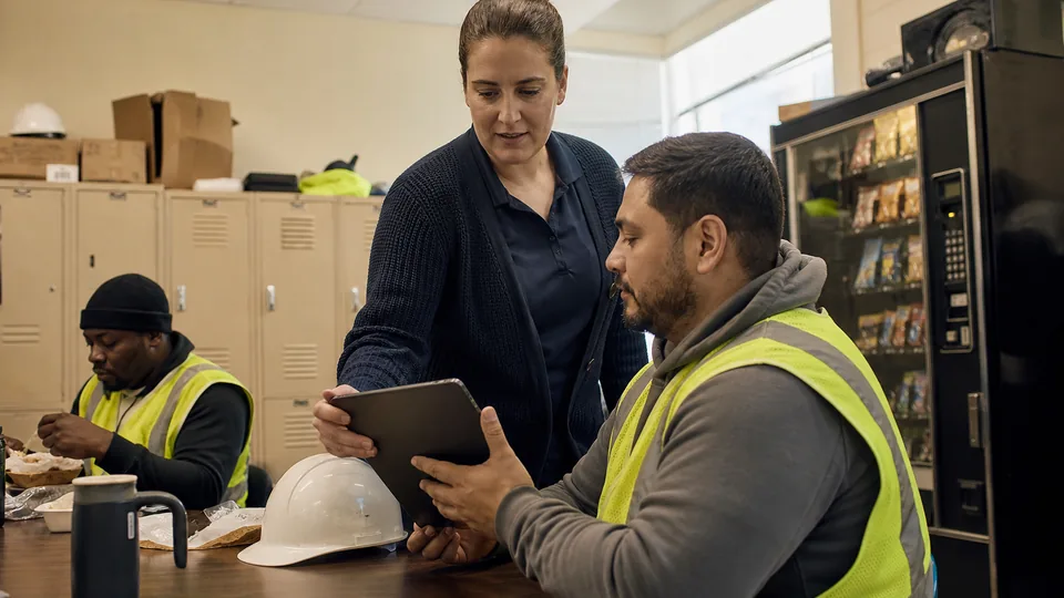 Compliance lead handing a tablet to a warehouse forklift operator for annual code of conduct training