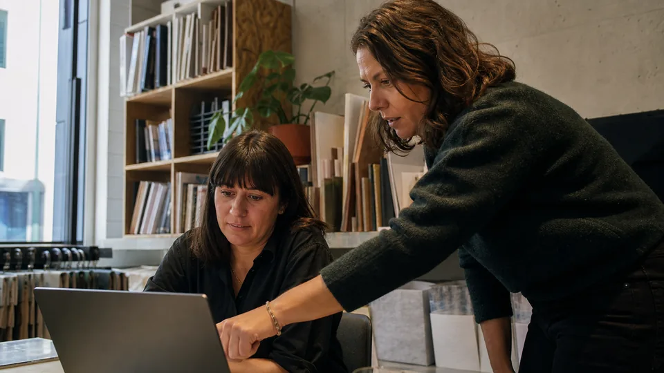 Operations manager walking a new employee through a workflow at a laptop