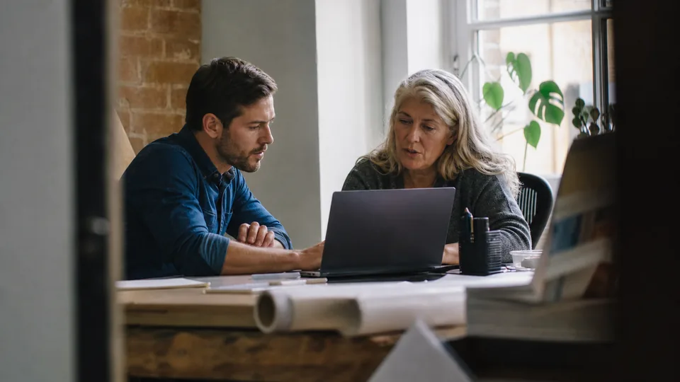 Two coworkers comparing training software options on one laptop